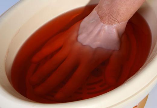 A woman dipping her hand in melted paraffin.